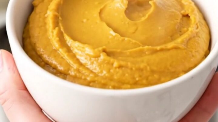 A warm, smooth pumpkin cheesecake dip in a white bowl with crackers ready for serving.