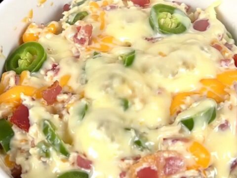 A top-down view of a black slow cooker filled with a creamy, bubbling bacon and corn dip on a white countertop.