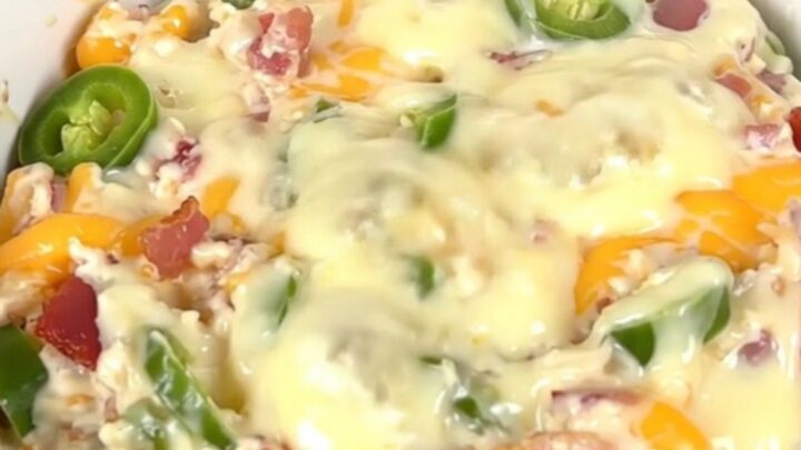A top-down view of a black slow cooker filled with a creamy, bubbling bacon and corn dip on a white countertop.