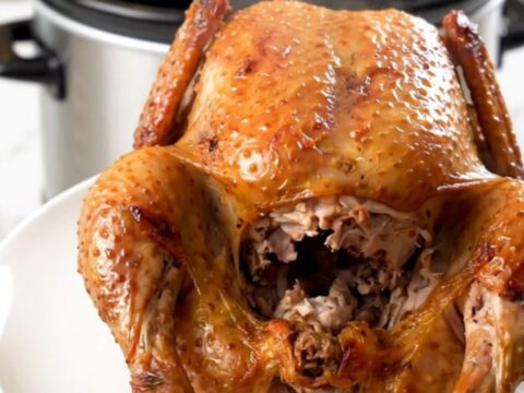 A golden-brown whole roasted chicken sits on a clean white plate, steaming slightly.