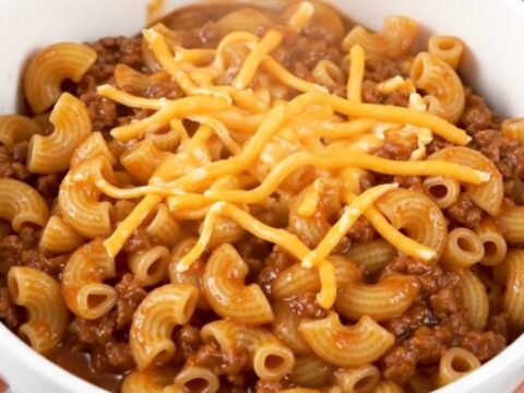 A steaming, glossy beef macaroni goulash in a plain white bowl, showcasing tender pasta and melted cheese.