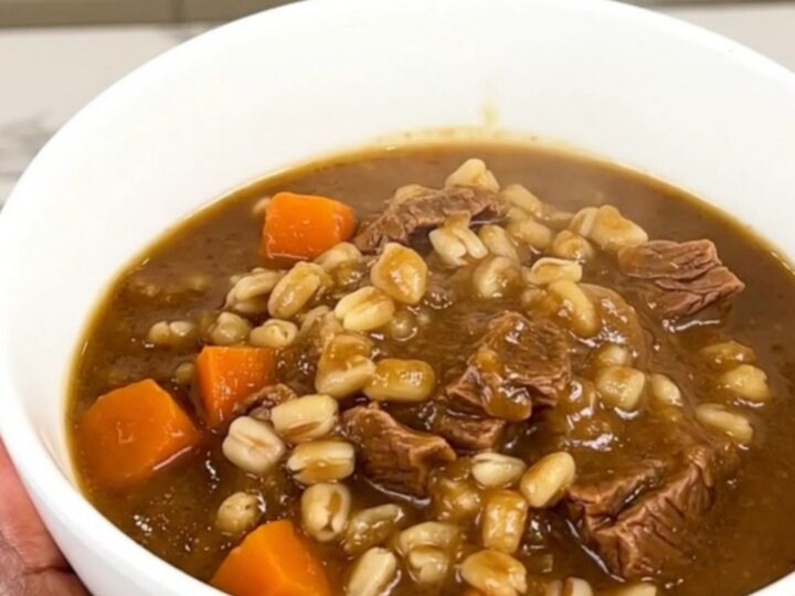 A close overhead shot of a black slow cooker filled with tender beef cubes, bright baby carrots, and a savory, dark broth.