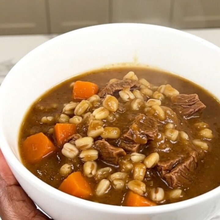 A close overhead shot of a black slow cooker filled with tender beef cubes, bright baby carrots, and a savory, dark broth.