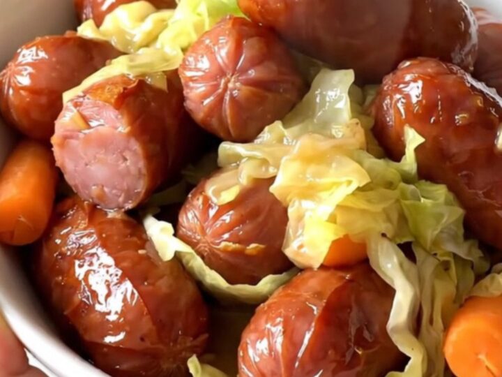 A white bowl filled with sliced smoked kielbasa, tender green cabbage wedges