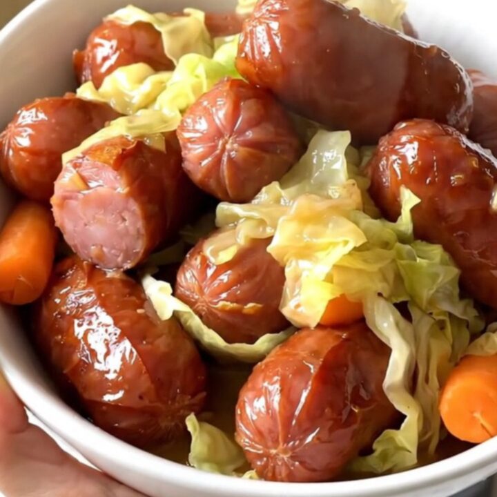 A white bowl filled with sliced smoked kielbasa, tender green cabbage wedges