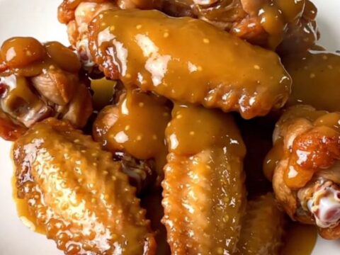 A top-down view of raw chicken wings and diced onions inside a black slow cooker on a white countertop.