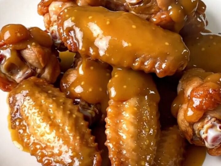 A top-down view of raw chicken wings and diced onions inside a black slow cooker on a white countertop.