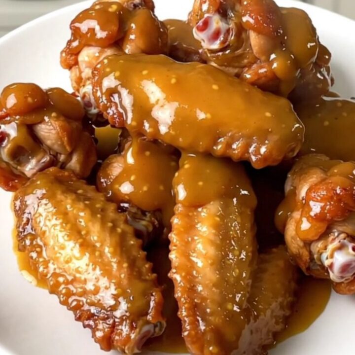 A top-down view of raw chicken wings and diced onions inside a black slow cooker on a white countertop.