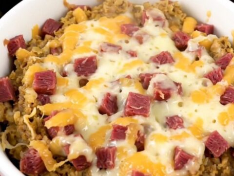 A close-up of a steaming, creamy hot Reuben dip in a white bowl with melted cheese and corned beef.