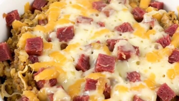 A close-up of a steaming, creamy hot Reuben dip in a white bowl with melted cheese and corned beef.