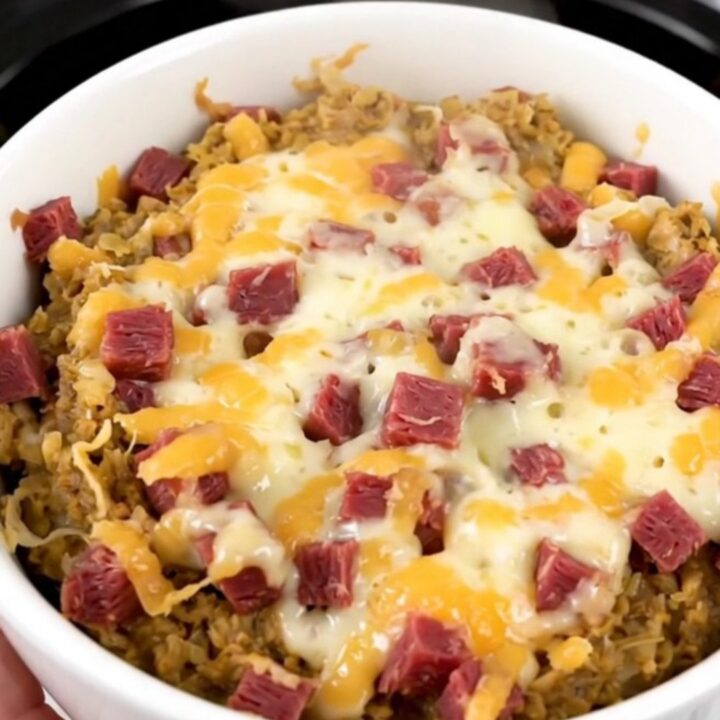 A close-up of a steaming, creamy hot Reuben dip in a white bowl with melted cheese and corned beef.