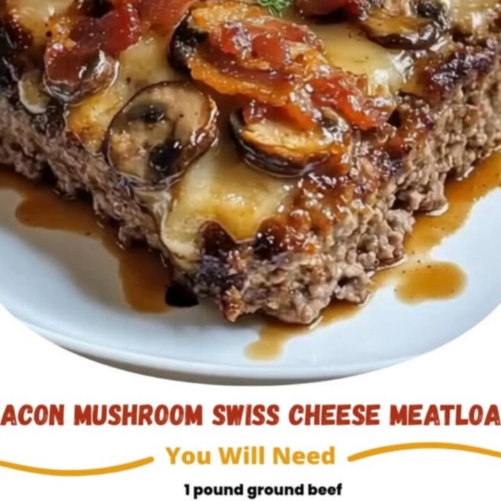Baked meatloaf slab topped with melted Swiss cheese, sautéed mushrooms, bacon, and thyme on a white plate.