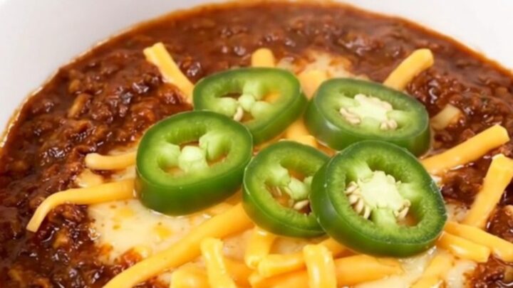 A steaming bowl of rich Texas beef chili topped with melted cheddar cheese and fresh jalapeño slices.