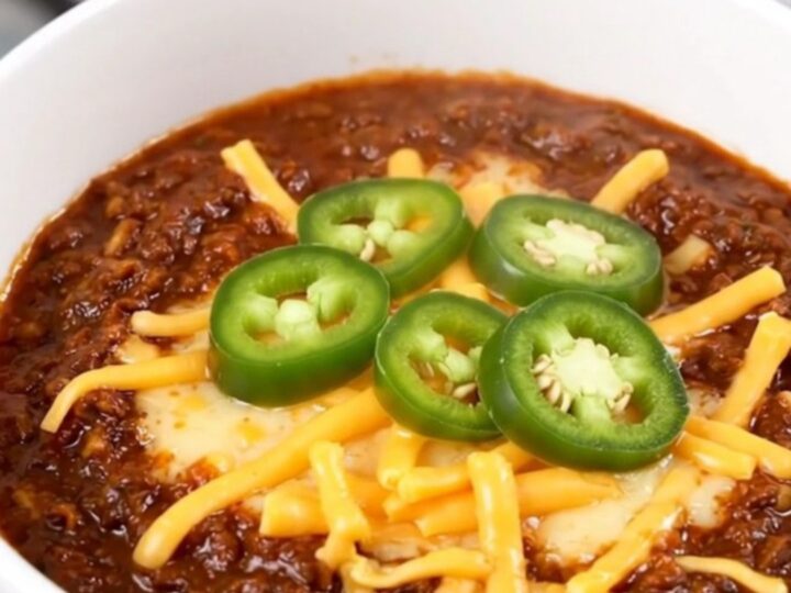 A steaming bowl of rich Texas beef chili topped with melted cheddar cheese and fresh jalapeño slices.