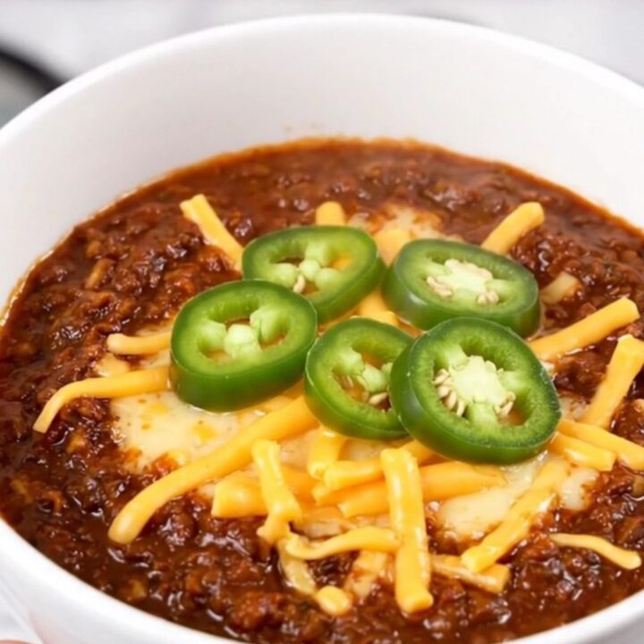 A steaming bowl of rich Texas beef chili topped with melted cheddar cheese and fresh jalapeño slices.