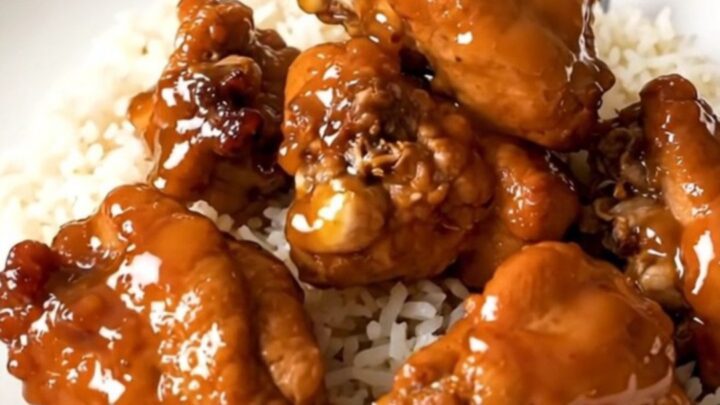 A top-down view of raw chicken pieces and orange marmalade inside a black slow cooker on a white speckled countertop.