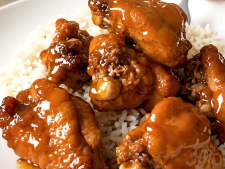 A top-down view of raw chicken pieces and orange marmalade inside a black slow cooker on a white speckled countertop.