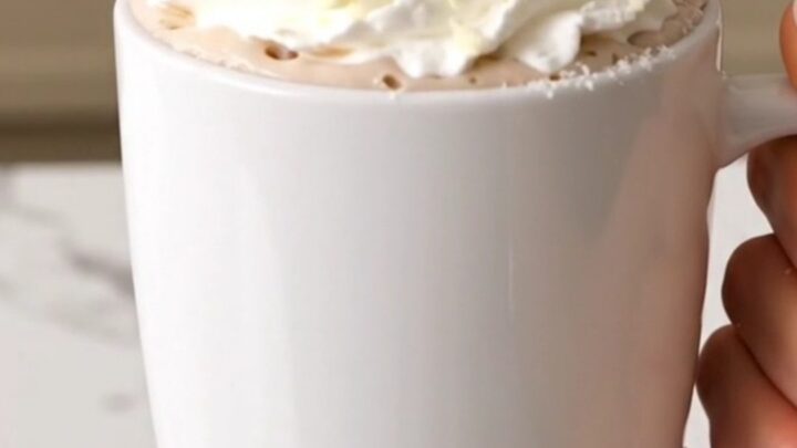 A slow cooker filled with creamy white hot chocolate on a white quartz countertop.