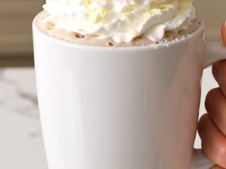A slow cooker filled with creamy white hot chocolate on a white quartz countertop.