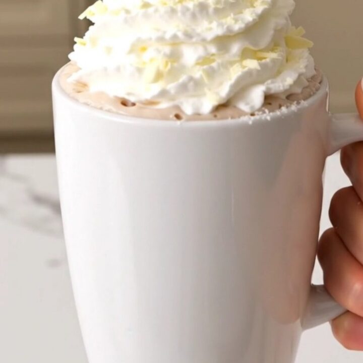 A slow cooker filled with creamy white hot chocolate on a white quartz countertop.