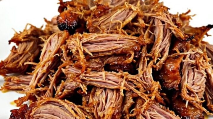 A close-up of a plate filled with shredded, glossy, and steaming Mexican carnitas pork.