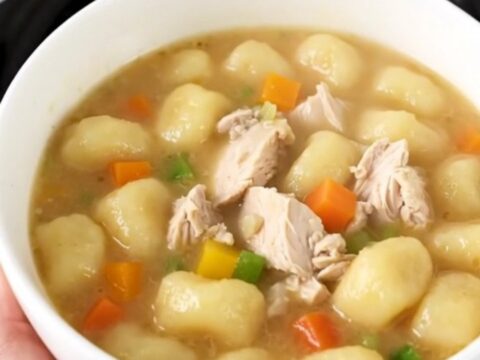 A close-up of a bowl of creamy chicken gnocchi soup with visible pieces of chicken and vegetables.