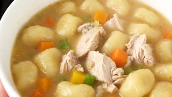 A close-up of a bowl of creamy chicken gnocchi soup with visible pieces of chicken and vegetables.
