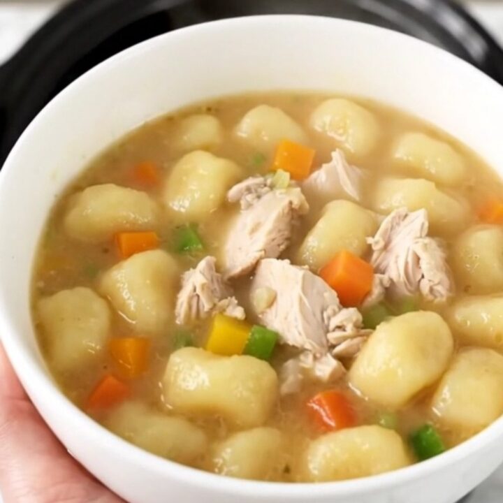 A close-up of a bowl of creamy chicken gnocchi soup with visible pieces of chicken and vegetables.