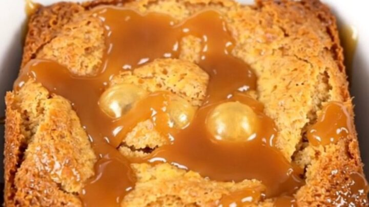 A warm slow cooker caramel apple dump cake with golden crust and visible pecans in a black crockpot.