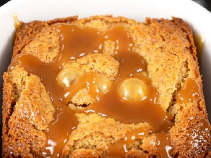 A warm slow cooker caramel apple dump cake with golden crust and visible pecans in a black crockpot.