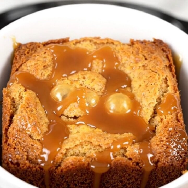 A warm slow cooker caramel apple dump cake with golden crust and visible pecans in a black crockpot.