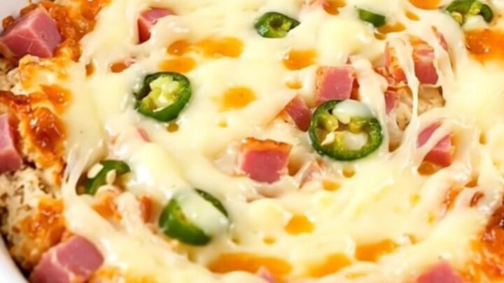 A close-up of a creamy, melted Mississippi Sin Dip in a white bowl, showing ham and chiles.