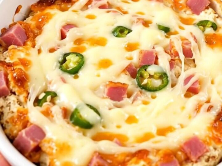 A close-up of a creamy, melted Mississippi Sin Dip in a white bowl, showing ham and chiles.