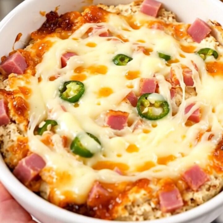A close-up of a creamy, melted Mississippi Sin Dip in a white bowl, showing ham and chiles.