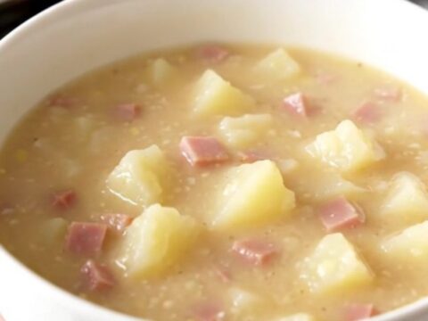 A white bowl filled with creamy ham and potato chowder sitting on a table.