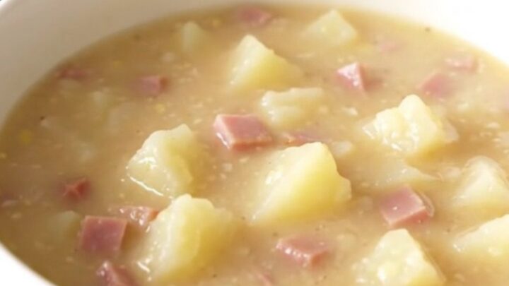 A white bowl filled with creamy ham and potato chowder sitting on a table.