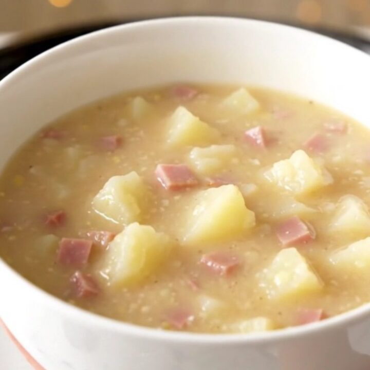 A white bowl filled with creamy ham and potato chowder sitting on a table.