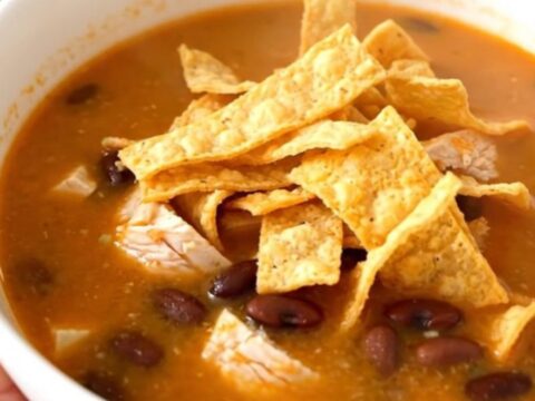 A white bowl filled with steaming chicken tortilla soup, topped with crispy tortilla strips and held by a hand.