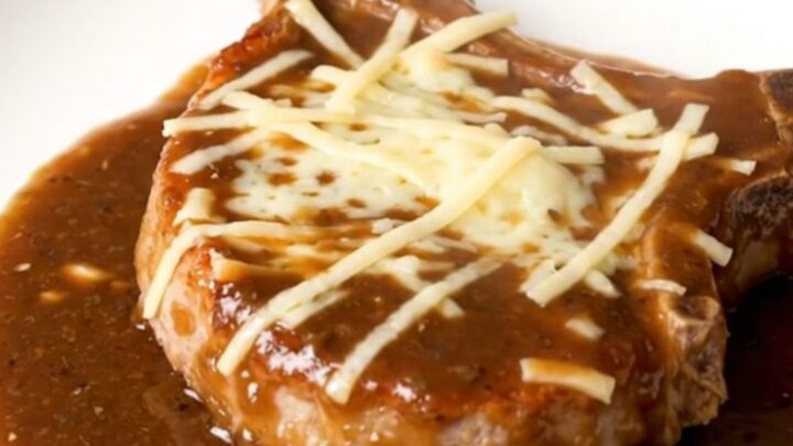 A finished slow cooker French onion pork chop topped with melted Swiss cheese and rich onion gravy on a white plate.