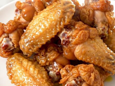 Golden, glossy lemon pepper chicken wings arranged neatly on a white plate with fresh parsley garnish.