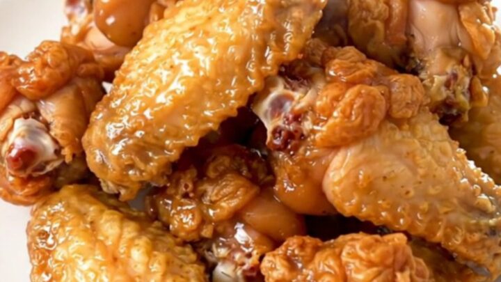 Golden, glossy lemon pepper chicken wings arranged neatly on a white plate with fresh parsley garnish.