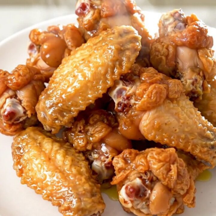 Golden, glossy lemon pepper chicken wings arranged neatly on a white plate with fresh parsley garnish.