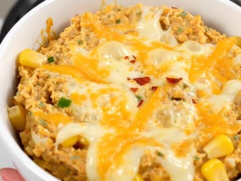 A warm, creamy Mexican street corn dip in a white bowl, garnished with chili powder and ready to eat.