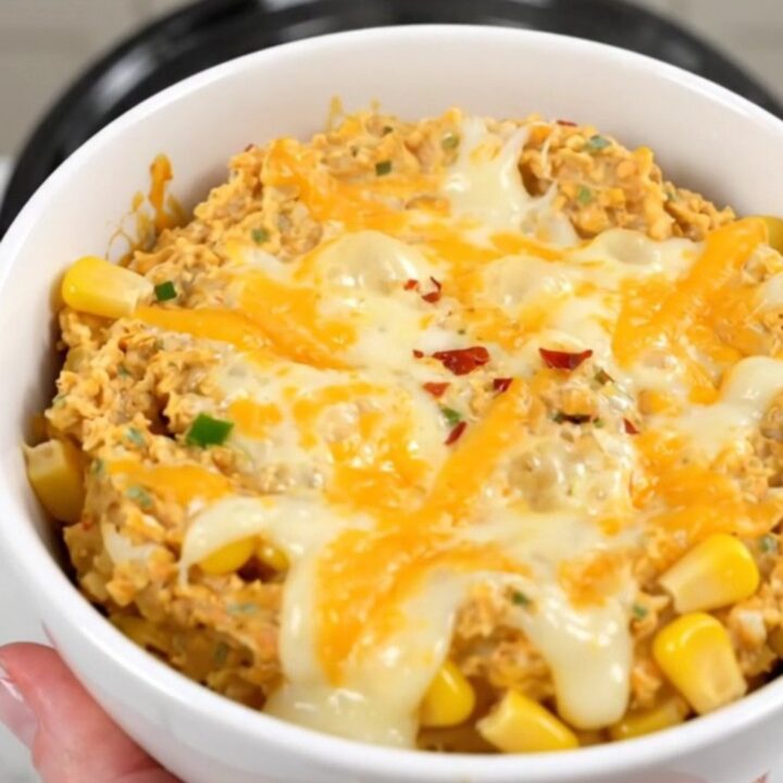 A warm, creamy Mexican street corn dip in a white bowl, garnished with chili powder and ready to eat.