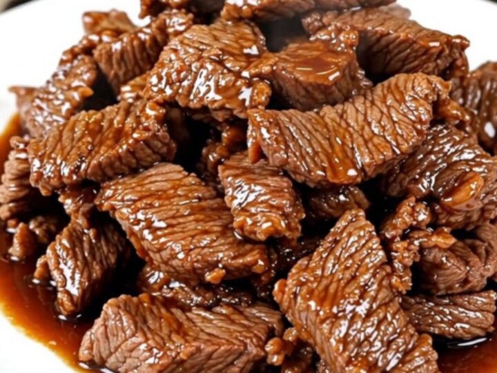 A close-up of tender, glossy Mongolian beef strips served on a white plate.