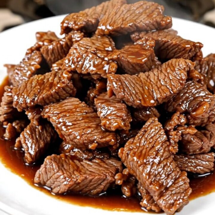 A close-up of tender, glossy Mongolian beef strips served on a white plate.
