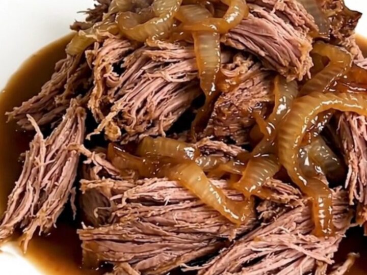 A close-up shot of a tender, shredded beef chuck roast in a slow cooker, featuring a rich barbecue glaze and sweet onions.