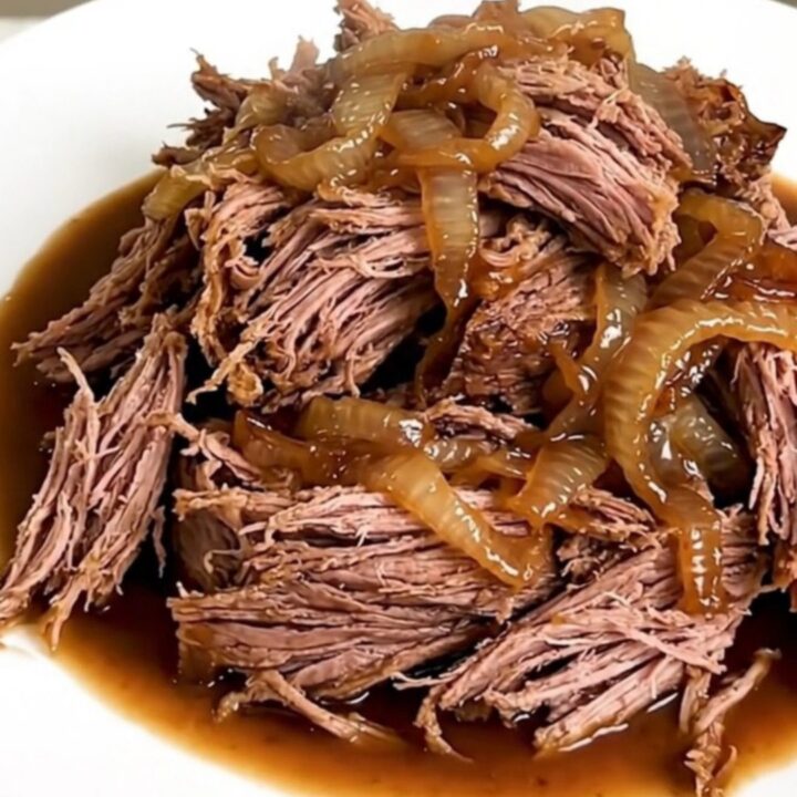 A close-up shot of a tender, shredded beef chuck roast in a slow cooker, featuring a rich barbecue glaze and sweet onions.