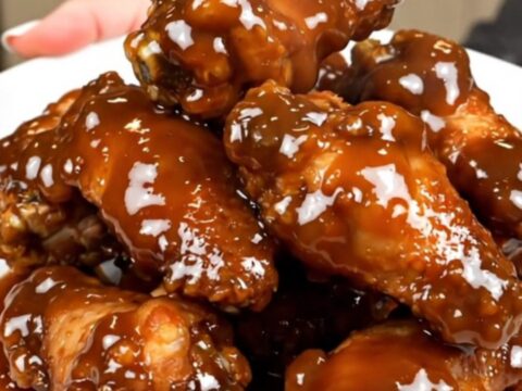 A close-up of sticky maple bacon chicken wings piled on a white plate.