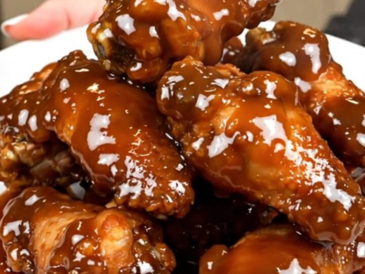 A close-up of sticky maple bacon chicken wings piled on a white plate.